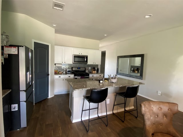 kitchen with white cabinets, appliances with stainless steel finishes, a kitchen island with sink, light stone counters, and a breakfast bar