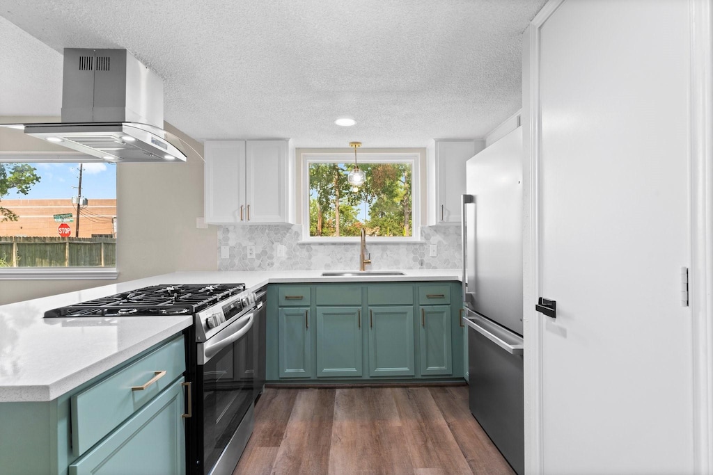 kitchen with island exhaust hood, appliances with stainless steel finishes, hanging light fixtures, white cabinets, and sink