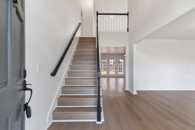 stairway with ceiling fan, french doors, a towering ceiling, and hardwood / wood-style flooring