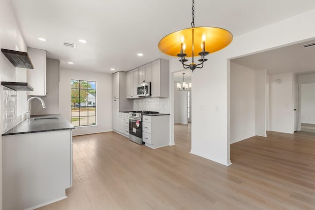 kitchen with pendant lighting, sink, appliances with stainless steel finishes, white cabinetry, and an inviting chandelier