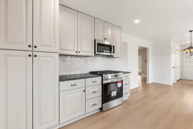 kitchen with an inviting chandelier, appliances with stainless steel finishes, white cabinets, light hardwood / wood-style floors, and backsplash