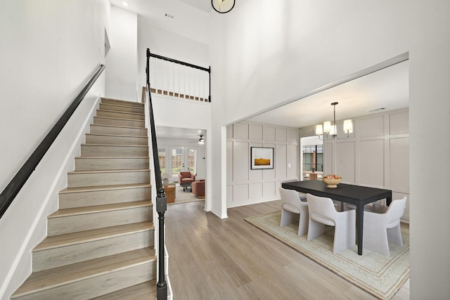 staircase featuring ceiling fan with notable chandelier, hardwood / wood-style floors, and a high ceiling