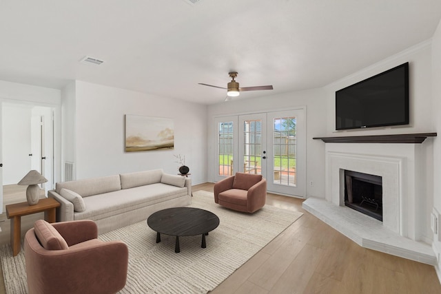 living room with french doors, ceiling fan, a fireplace, and light hardwood / wood-style flooring