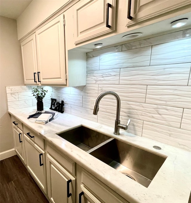 kitchen with light stone counters, baseboards, dark wood finished floors, a sink, and decorative backsplash