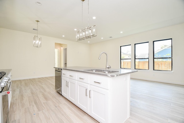 kitchen featuring sink, decorative light fixtures, white cabinetry, gas range oven, and a center island with sink