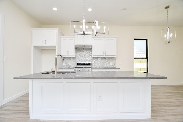 kitchen featuring hanging light fixtures, range, a spacious island, backsplash, and sink