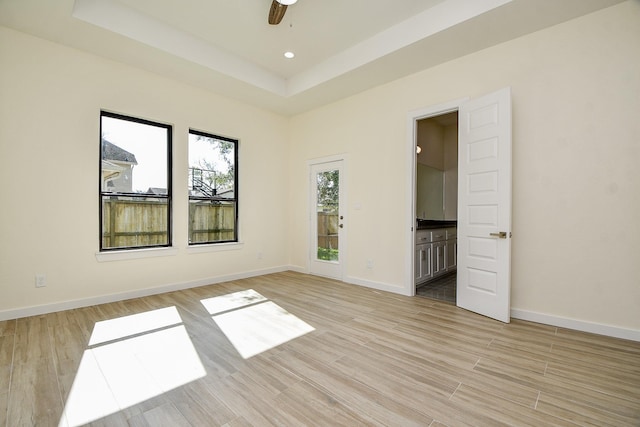 unfurnished bedroom with ceiling fan, light hardwood / wood-style floors, connected bathroom, and a raised ceiling