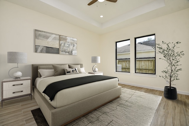 bedroom with ceiling fan, a tray ceiling, and wood-type flooring