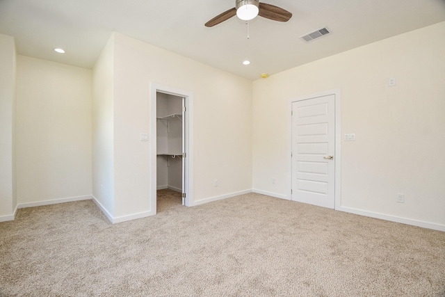 unfurnished bedroom featuring a closet, a walk in closet, light carpet, and ceiling fan