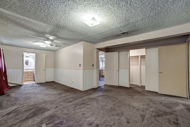 unfurnished living room with a textured ceiling, ceiling fan, and dark colored carpet