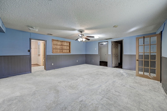 carpeted spare room with a textured ceiling, ceiling fan, and wood walls