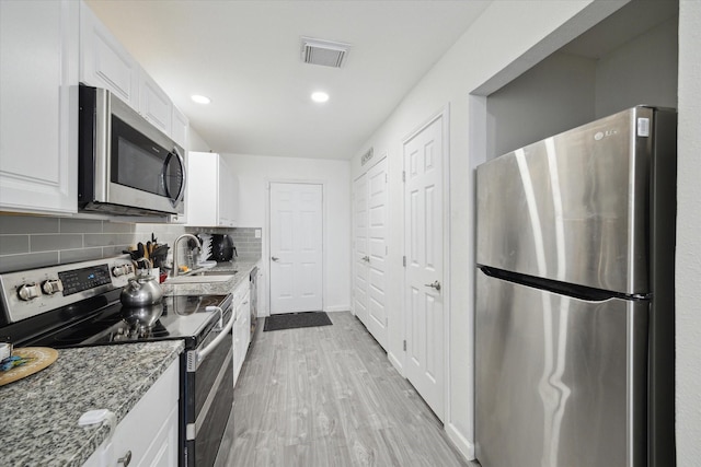 kitchen with light stone counters, appliances with stainless steel finishes, white cabinetry, and sink