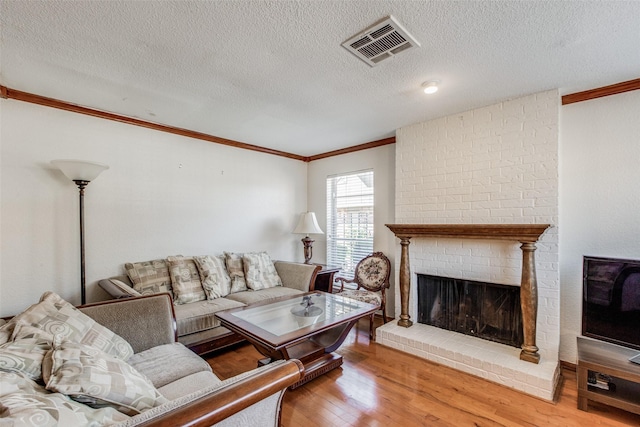 living room with a brick fireplace, a textured ceiling, hardwood / wood-style flooring, and crown molding