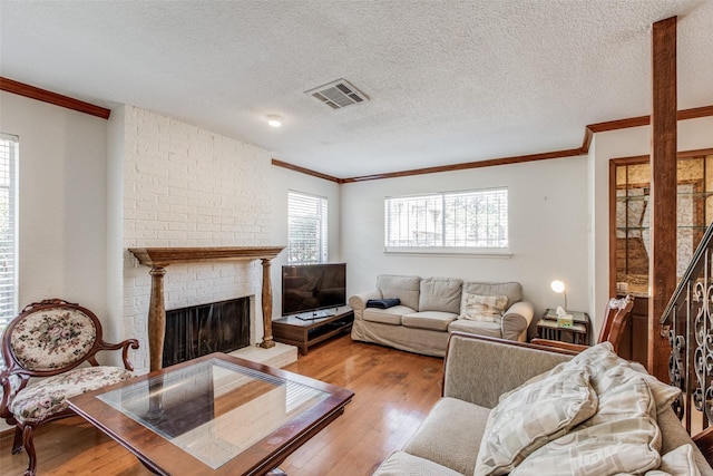 living room with a brick fireplace, a textured ceiling, light hardwood / wood-style floors, and ornamental molding