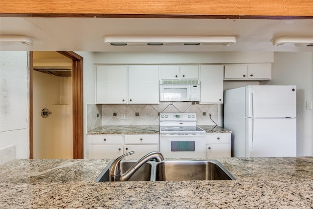 kitchen with white appliances, light stone counters, decorative backsplash, sink, and white cabinetry