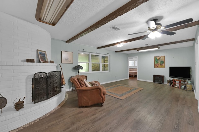 living room with a textured ceiling, a fireplace, ceiling fan, hardwood / wood-style flooring, and beam ceiling