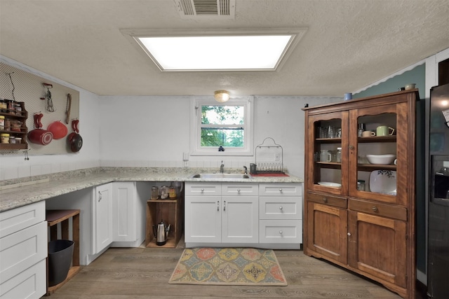 kitchen featuring sink, white cabinetry, light wood-type flooring, and light stone counters