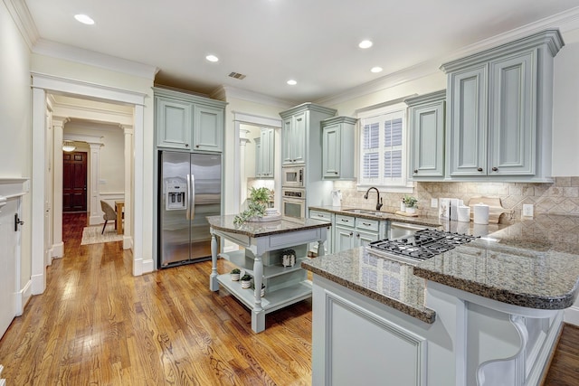 kitchen featuring sink, a center island, light wood-type flooring, dark stone countertops, and appliances with stainless steel finishes