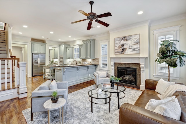 living room with ceiling fan, a high end fireplace, light hardwood / wood-style flooring, and ornamental molding