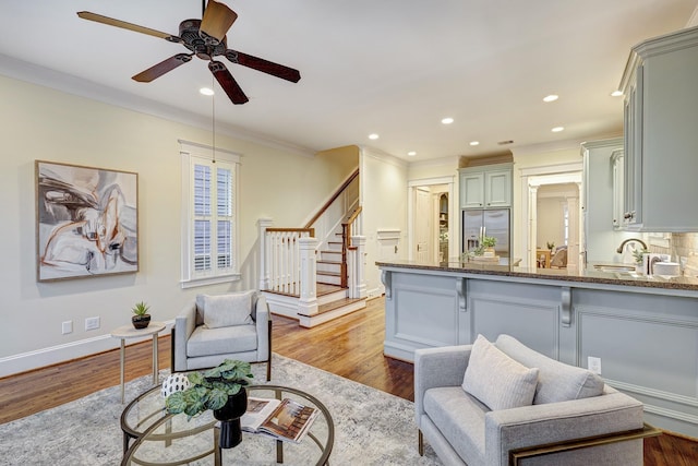 living room with crown molding, ceiling fan, sink, and light wood-type flooring