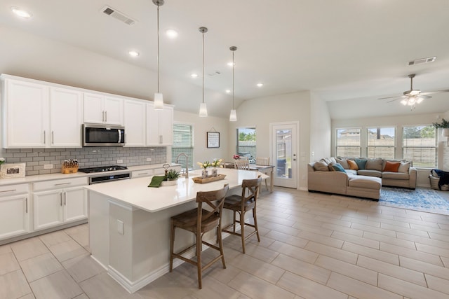 kitchen featuring white cabinetry, a kitchen bar, a center island with sink, appliances with stainless steel finishes, and decorative light fixtures