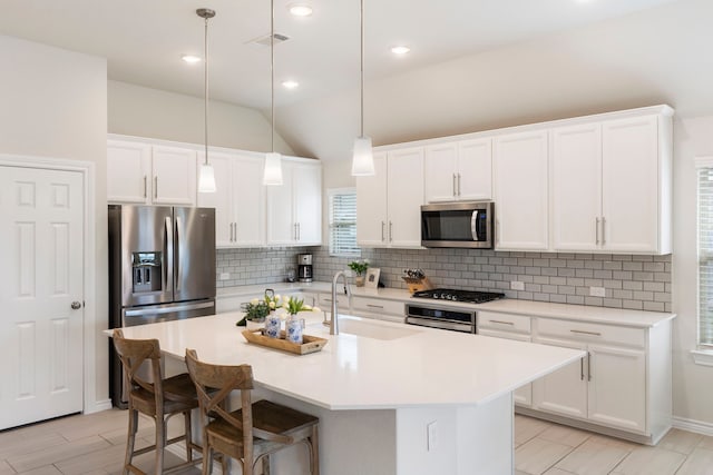 kitchen with vaulted ceiling, sink, white cabinetry, a kitchen island with sink, and stainless steel appliances