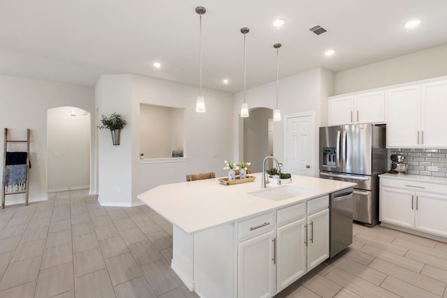 kitchen with pendant lighting, white cabinetry, stainless steel appliances, an island with sink, and sink