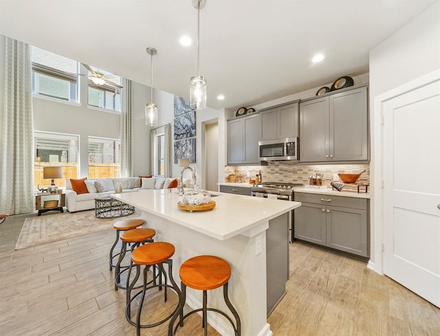 kitchen featuring a kitchen bar, light wood-style flooring, gray cabinets, a sink, and appliances with stainless steel finishes