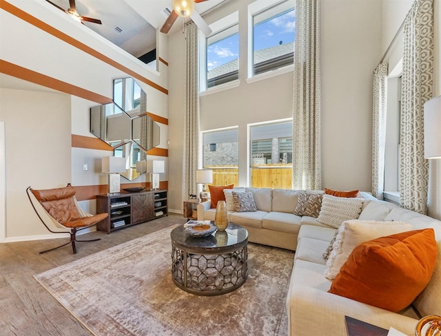 living room featuring a towering ceiling, baseboards, ceiling fan, and wood finished floors