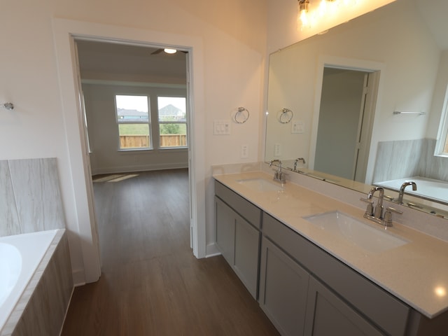 597 Copper Springs Dr, Magnolia, TX 77354 - bathroom featuring wood finished floors, double vanity, a garden tub, and baseboards