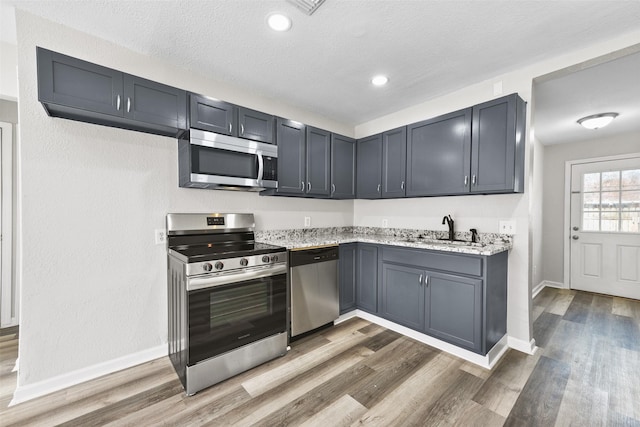 kitchen with appliances with stainless steel finishes, light stone counters, hardwood / wood-style flooring, a textured ceiling, and sink