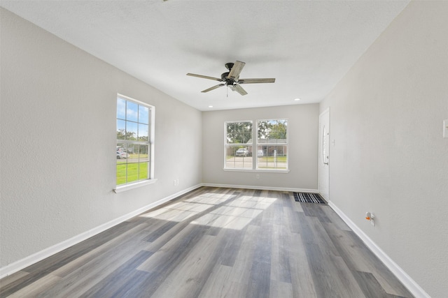 empty room with ceiling fan, a wealth of natural light, and hardwood / wood-style floors