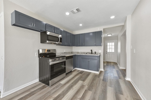 kitchen featuring stainless steel appliances, sink, hardwood / wood-style floors, light stone countertops, and gray cabinets