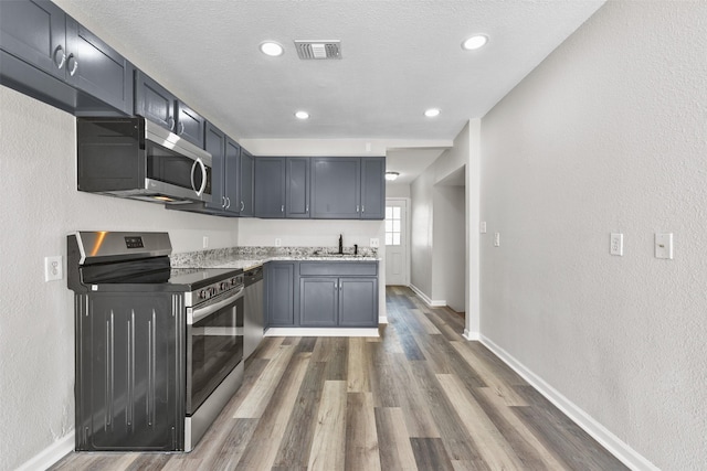 kitchen with sink, a textured ceiling, light stone counters, dark hardwood / wood-style floors, and appliances with stainless steel finishes