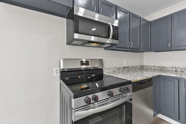 kitchen featuring appliances with stainless steel finishes, gray cabinetry, and light stone counters