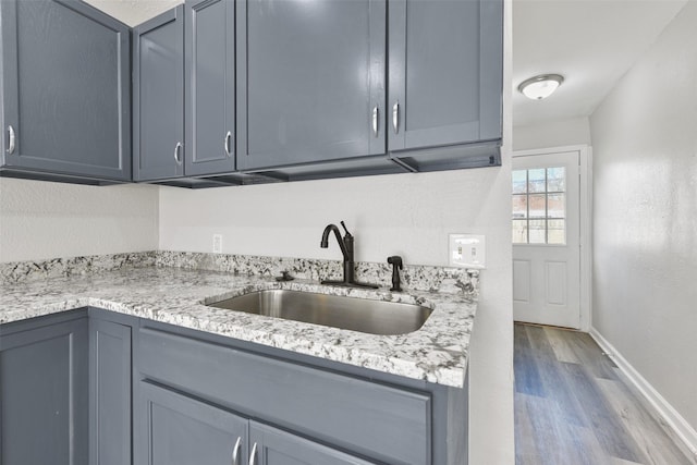 kitchen featuring sink, light wood-type flooring, gray cabinets, and light stone countertops