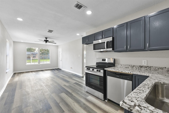 kitchen with stainless steel appliances, light stone countertops, ceiling fan, hardwood / wood-style flooring, and a textured ceiling