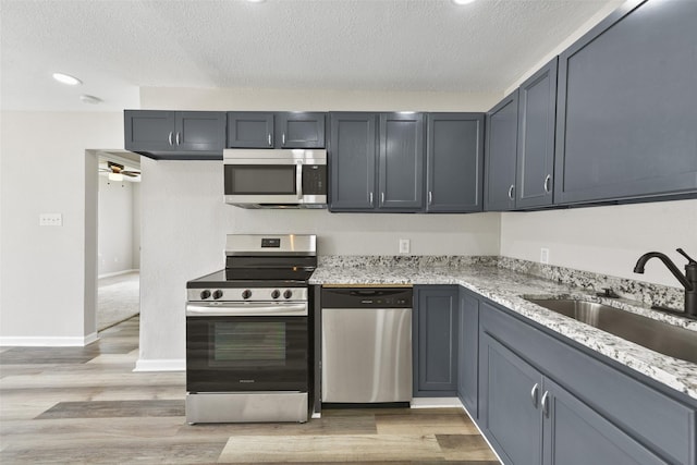 kitchen featuring light stone countertops, light hardwood / wood-style flooring, appliances with stainless steel finishes, ceiling fan, and sink