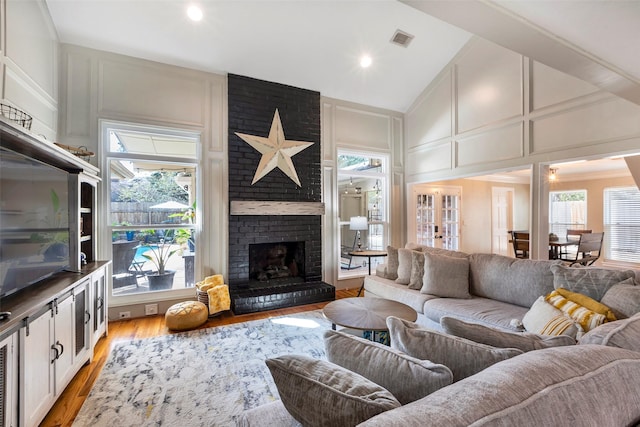 living room featuring light hardwood / wood-style flooring, a brick fireplace, and high vaulted ceiling