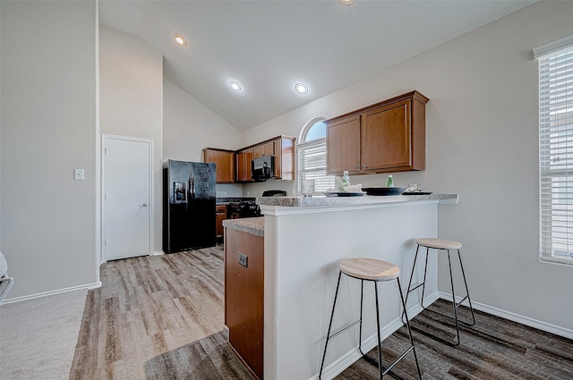 kitchen with kitchen peninsula, light hardwood / wood-style flooring, black appliances, high vaulted ceiling, and a breakfast bar area