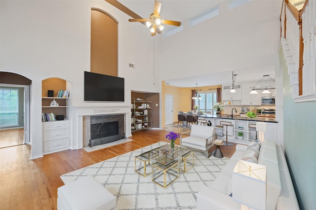 living room featuring sink, a towering ceiling, a tiled fireplace, ceiling fan, and built in features