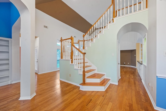 staircase with built in features, a towering ceiling, and wood-type flooring