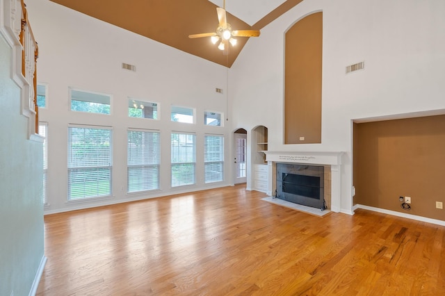 unfurnished living room featuring ceiling fan, light hardwood / wood-style floors, a towering ceiling, and a fireplace