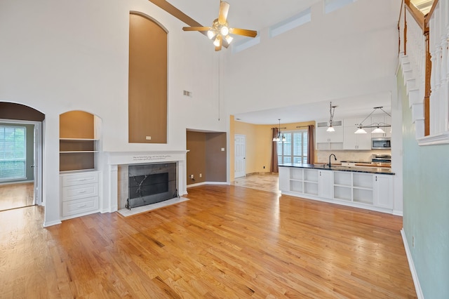 unfurnished living room with a towering ceiling, ceiling fan, a fireplace, sink, and light hardwood / wood-style flooring