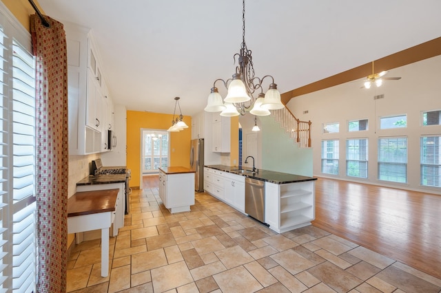 kitchen featuring white cabinets, a center island, ceiling fan with notable chandelier, pendant lighting, and appliances with stainless steel finishes