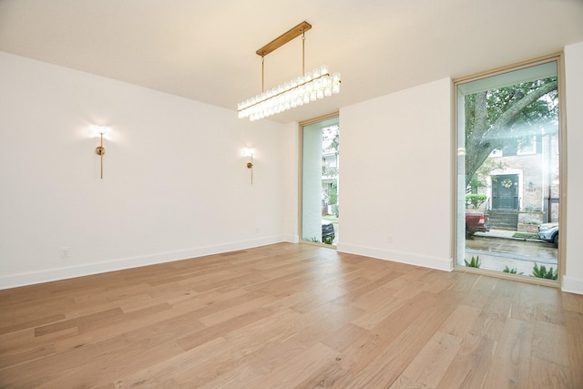 empty room with light hardwood / wood-style flooring, an inviting chandelier, and a wealth of natural light