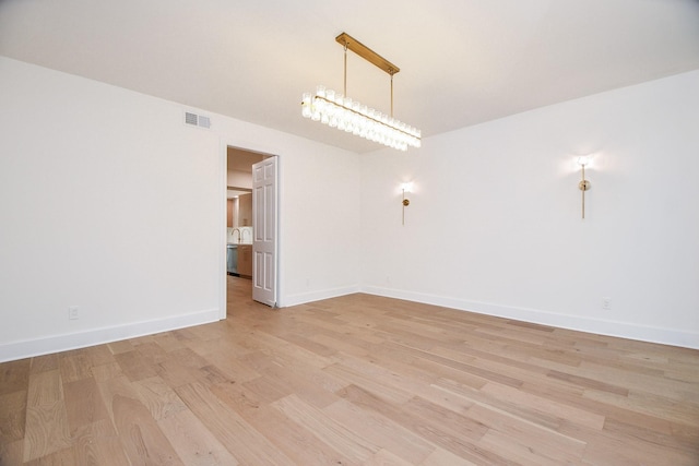 spare room featuring light wood-type flooring and a chandelier