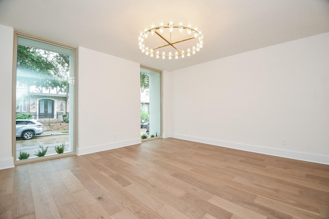 unfurnished room with light hardwood / wood-style floors, an inviting chandelier, and a healthy amount of sunlight