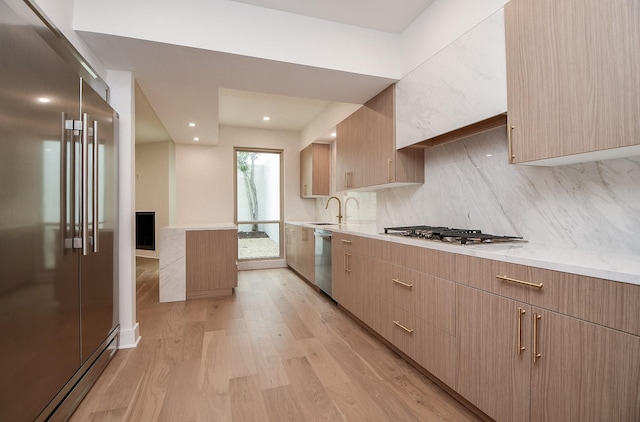 kitchen with light stone countertops, light hardwood / wood-style flooring, stainless steel appliances, light brown cabinetry, and tasteful backsplash