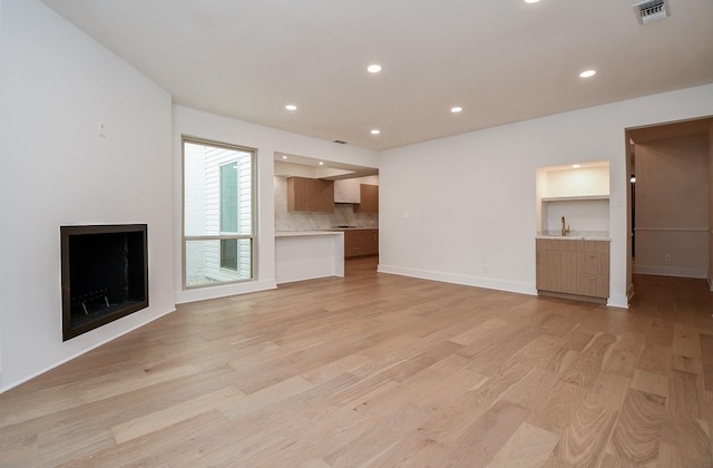 unfurnished living room featuring sink and light hardwood / wood-style floors